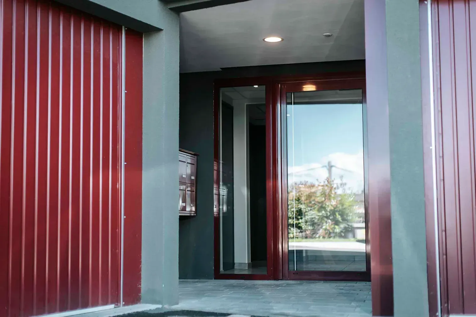 Entrée d’un bâtiment au bardage métallique rouge, encadrement de porte sur mesure